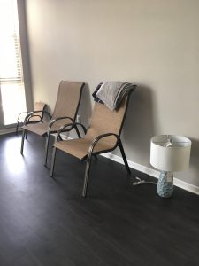 empty apartment living room with just two patio chairs and a lamp on the floor