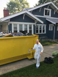man in coveralls walking beside dumpster filled with contents of home exposed to toxic mold