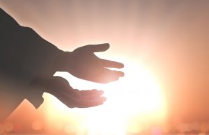 the healing hands of jesus reaching out in front of a bight sun to symbolize hope