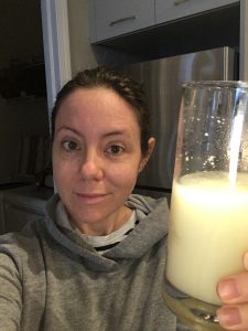 woman in sweatshirt holding glass milky liquid which is an elemental diet formula