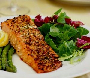 baked salmon on a plate with greens, asparagus, and lemon wedges