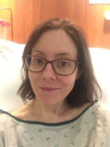 thin woman in hospital gown sitting on a hospital bed while there for ulcertaive colitis flare