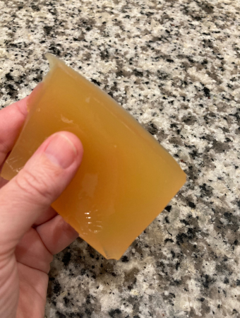 Hand holding golden piece of jello made from unfiltered apple juice and beef gelatin